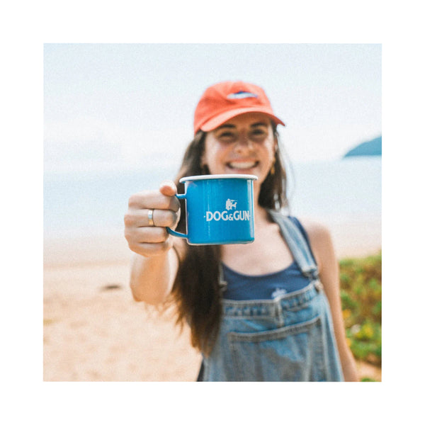 Blue/350ml | Dog & Gun Enamel Mug Image Showing The Mug Being Held At The Beach.