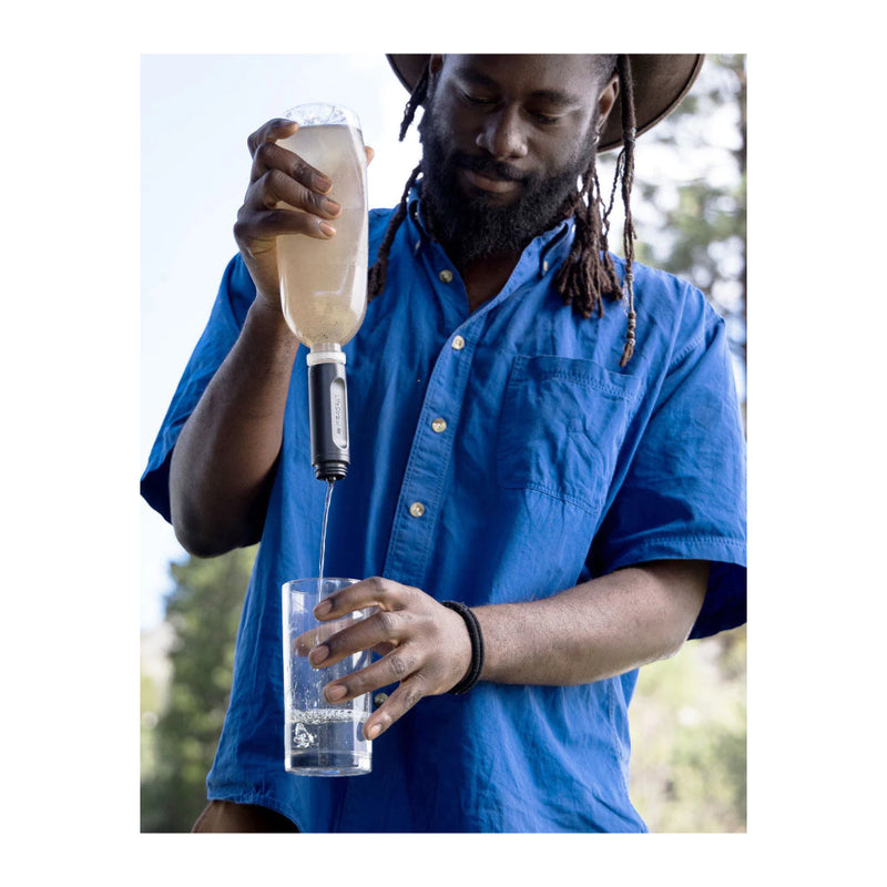 Mountain Blue | LifeStraw Peak Collapsible Squeeze Bottle 1L Image Showing Model Using A Plastic Bottle With Filter Screwed On To Pour Water Into A Glass.