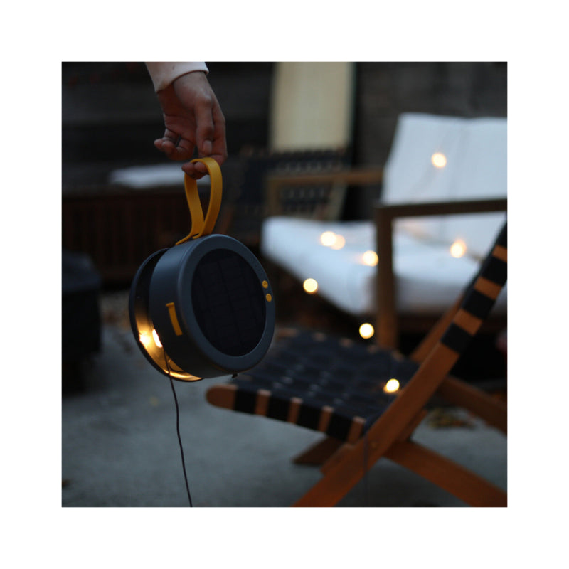 Luci Light String Light Plus | Image Displaying String Lights Strung Across Chairs, Power Hub Being Carried By Handle.