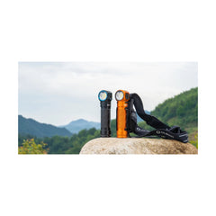 Black | Olight Perun 3 Rechargeable Headlamp 3000lms Image Showing Black Torch Out Of Cradle Standing On A Rock , Orange Torch In Cradle Standing On A Rock.
