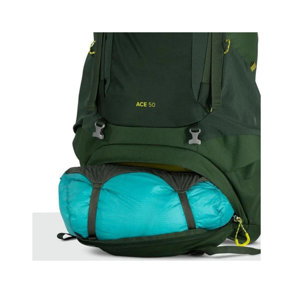 Green Canopy | Osprey Ace Backpack Image Showing Close Up View of The Bottom Front Pocket, Open With A Sleeping Bag Inside.