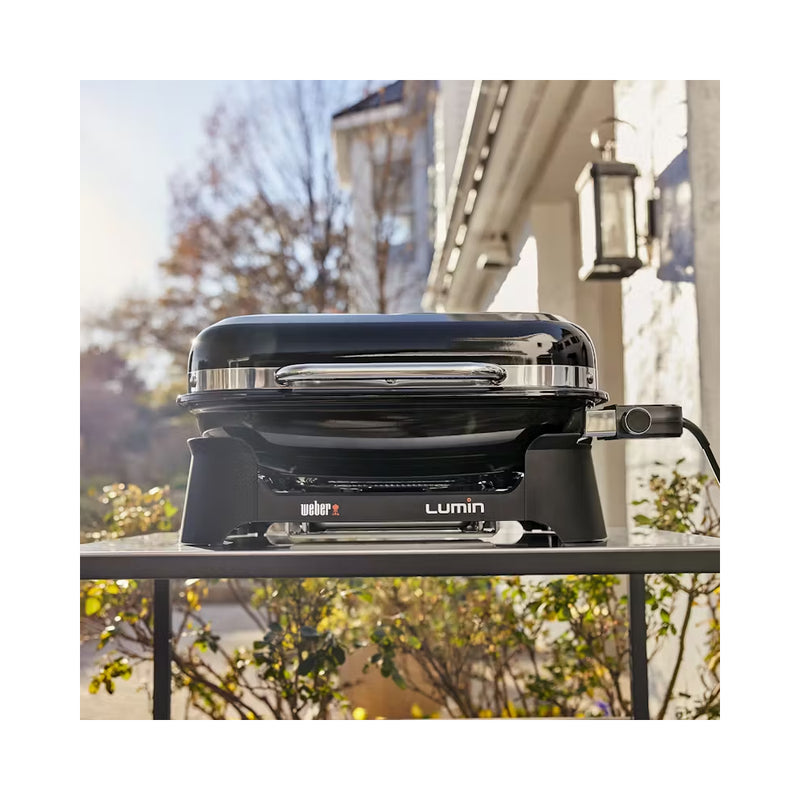 Black | Weber Lumin Electric BBQ With Stand And Side Table image Showing BBQ Out Side On A Table.