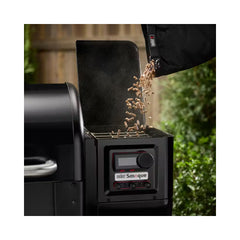 Black | Weber Smoque XL Pellet Smoker  Image Showing Close Up Pellets Being Poured Into The Pellet Box.