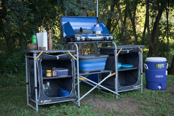 Kitchen set up and in use on grassy camp site with trees in the background
