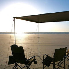 Awning set up with chairs under at a beach with the sun on the horizon