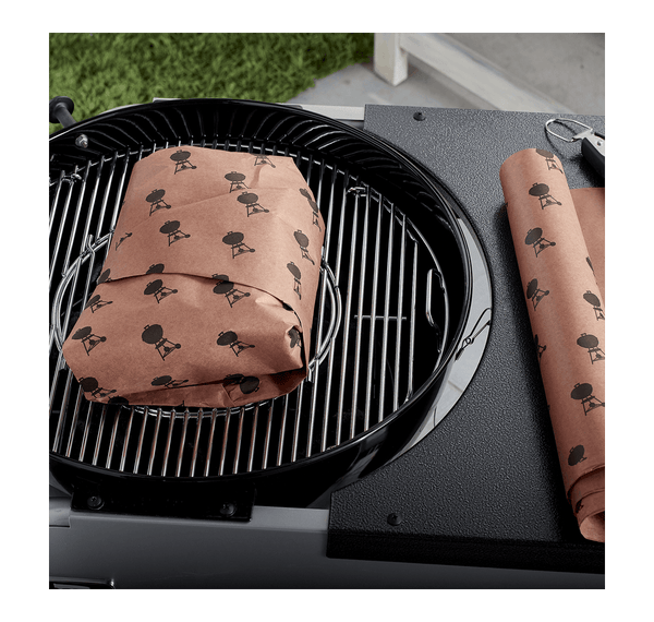 Paper wrapped item on charcoal bbq with roll on the table next to it